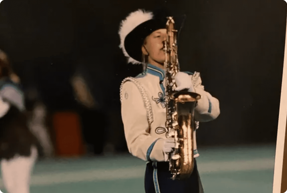 Marching band member playing saxophone during performance.