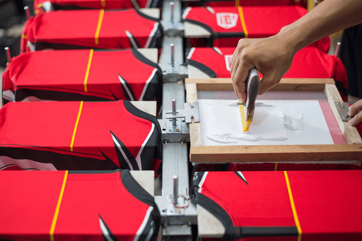 A person using a squeegee to screen print red t-shirts.