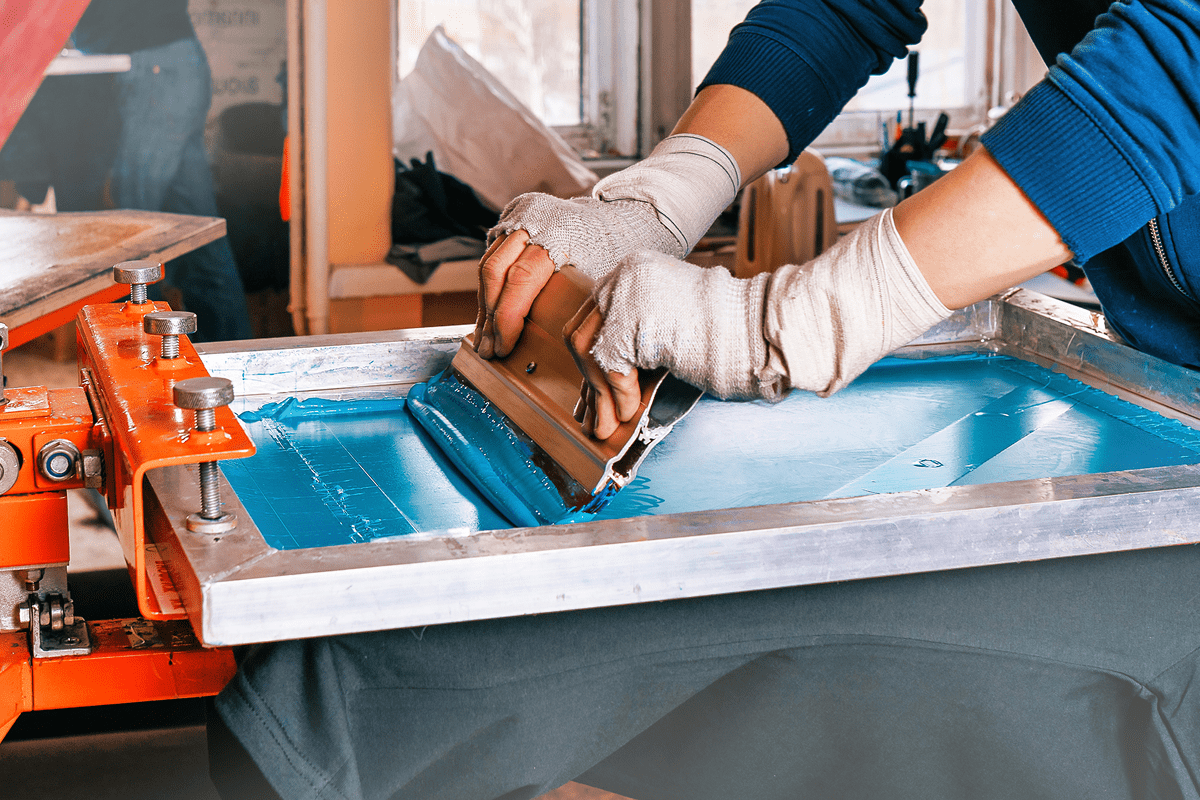 A person screen printing blue ink onto fabric using a squeegee.